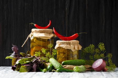 Téléchargez les photos : Pickled cucumbers in a jar, fresh gherkins, red and green chili, dill, basil, garlicn on a dark wooden background. Peppers, onions and fresh gherkins for preservation. Cucumber salad. - en image libre de droit