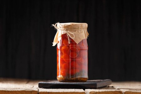 Téléchargez les photos : Tomates cerises marinées dans des bocaux en verre avec couvercles artisanaux avec poivre, aneth, ail sur un fond en bois close-up. Composition des tomates en conserve maison - en image libre de droit
