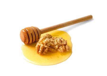 Téléchargez les photos : Plusieurs noix et une trempette en bois se trouvent dans une goutte de miel sur un fond blanc en gros plan. Grandes noix et miel isolés sur fond blanc. - en image libre de droit