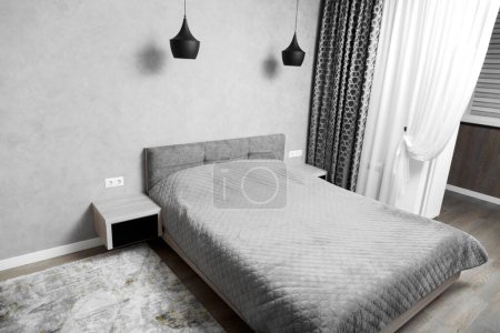 Téléchargez les photos : Design moderne de la chambre dans des tons gris, minimalisme à l'intérieur. Un grand lit dans la chambre, tables de chevet avec verre noir, lustres noirs, tapis. - en image libre de droit