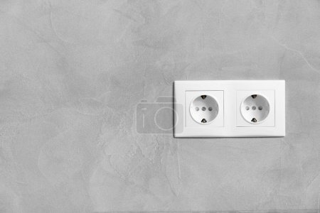 Téléchargez les photos : Doubles prises électriques en plastique blanc sur mur de texture grise close-up avec espace pour le texte. - en image libre de droit