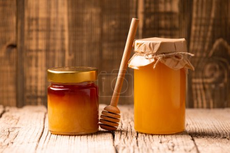 Téléchargez les photos : Sarrasin et miel de fleurs dans des pots fermés en verre et une trempette en bois sur un fond en bois. Le concept de produits apicoles biologiques. - en image libre de droit