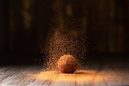 Cocoa powder is sprinkled on a chocolate truffle under a beautiful light. A ball of chocolate truffle is sprinkled with cocoa on a dark background close-up. Conceptual photo of a gourmet truffle.