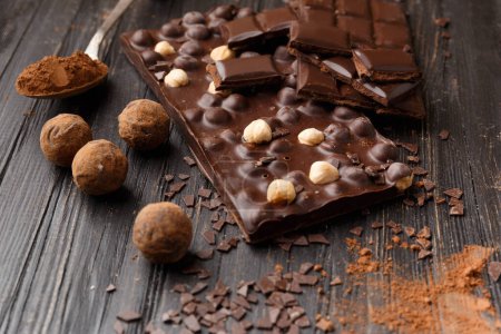Téléchargez les photos : Chocolat artisanal aux noisettes, morceaux de chocolat noir, cacao dans une cuillère vintage, truffes au chocolat sur fond bois foncé. Concept de variété de chocolat. - en image libre de droit
