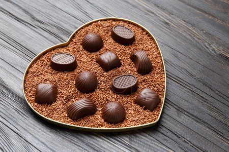 Photo for Chocolate candies in chocolate chips in a heart-shaped box on a dark wooden background top view, Valentine's Day. - Royalty Free Image