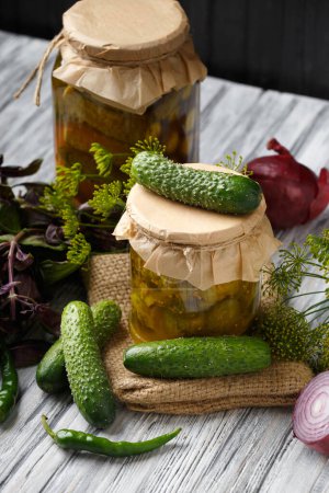 Photo for Canned cucumbers in a jar, pickled sliced cucumber salad, fresh gherkins, hot peppers, basil, onions on a wooden background. Homemade canned vegetables. - Royalty Free Image