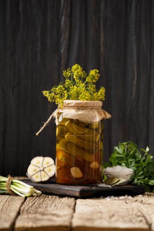 Foto de Pepinos enlatados caseros en un frasco, ajo, especias y hierbas para la marinada sobre un fondo de madera. - Imagen libre de derechos