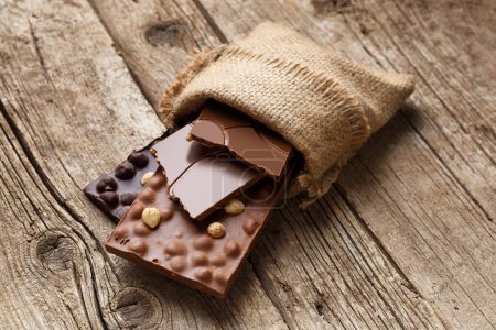 Téléchargez les photos : Chocolat noir et au lait fait à la main avec noisettes dans un sac en toile de jute sur un fond en bois vieilli. Concept de chocolat fait main. - en image libre de droit