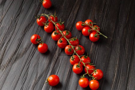 Foto de Cherry tomatoes on a branch on a dark wooden background top view. Fresh cherry tomatoes on a wooden background. Healthy food. Veganism. - Imagen libre de derechos