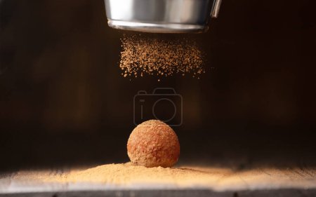 Photo for A ball of chocolate truffle is sprinkled with cocoa from a sieve on a dark background close-up. Chocolate sweets handmade. Conceptual photo of an exquisite truffle. - Royalty Free Image
