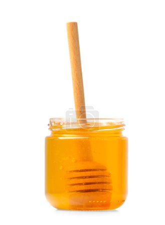 Photo for Organic honey in a glass transparent jar with a wooden dipper inside the jar on a white background. The honey stick lies inside a transparent jar of honey. Healthy bee products. - Royalty Free Image