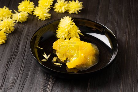 Photo for Crystallized honey in a black round plate and yellow flowers on a dark wooden background. - Royalty Free Image