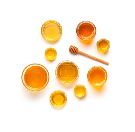 Foto de Composición creativa de tarros de miel y cazo de madera en vista superior aislamiento. Miel en un recipiente de vidrio de diferentes tamaños y un palo para miel sobre un fondo blanco. - Imagen libre de derechos