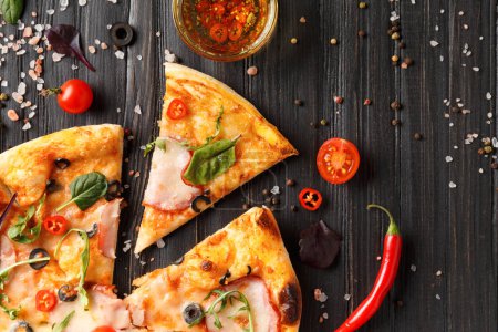 Foto de Pizza con carne seca, queso, rebanadas de pizza, salsa, verduras frescas y especias sobre un fondo de madera oscura, vista superior. - Imagen libre de derechos