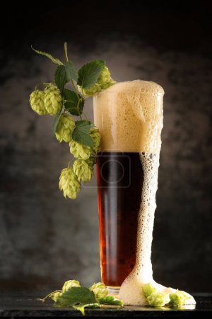 Photo for Dark beer in a mug and green hop on wooden table on brown background. The concept of natural beer. Brewing traditions. Oktoberfest. Beer Festival. St.Patrick 's Day - Royalty Free Image