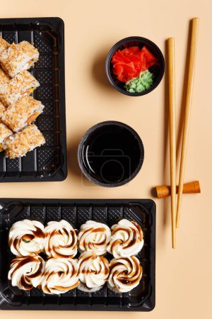 Foto de Un conjunto de rollos de sushi en paquetes de plástico para llevar con salsa de soja, jengibre, wasabi y palillos chinos sobre un fondo claro, vista superior. Entrega de sushi en un recipiente de plástico - Imagen libre de derechos