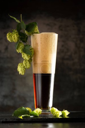 Photo for Dark beer in a mug and green hop on wooden table on brown background. The concept of natural beer. Brewing traditions. Oktoberfest. Beer Festival. St.Patrick 's Day - Royalty Free Image
