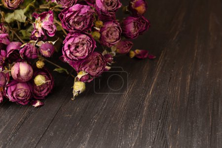 Foto de Bouquet of dry pink roses on a dark wooden background close-up. Concept of loneliness or age. Sadness, unhappy love. - Imagen libre de derechos