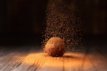 Photo for Cocoa powder is sprinkled on a chocolate truffle under a beautiful light. A ball of chocolate truffle is sprinkled with cocoa on a dark background close-up. Conceptual photo of a gourmet truffle. - Royalty Free Image