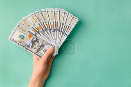 A lot of bills of 100 dollars in hands are folded in a fan on a green background top view with space for text. Currency, banknotes in female hands. The concept of success, business, wealth.