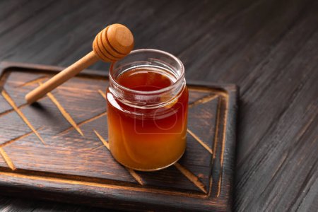 Photo for Honey in a jar and a wooden dipper on a dark wooden board on a textured background. Buckwheat honey on a dark background. - Royalty Free Image