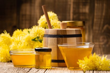 Foto de Composición creativa de miel en un frasco de vidrio y un tazón, una cazuela de madera y flores amarillas sobre un fondo de madera envejecida. El concepto de productos de abejas orgánicas. - Imagen libre de derechos