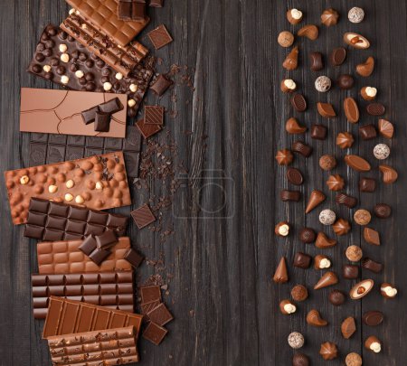 Foto de Varios dulces de chocolate oscuro y leche y palitos de chocolate, trufas de chocolate sobre una textura de madera oscura vista superior de fondo. - Imagen libre de derechos