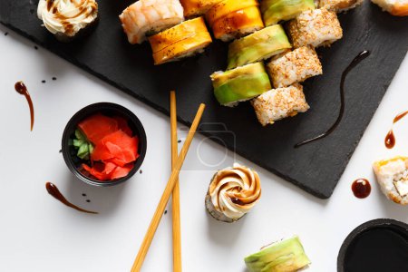 Foto de Conjunto de rollo con salmón, aguacate y anguila en un tablero de piedra con wasabi y salsa de soja sobre un fondo gris vista superior - Imagen libre de derechos