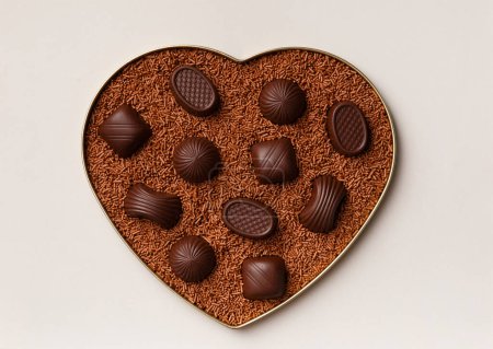 Téléchargez les photos : Boîte en forme de coeur avec des chocolats et des pépites de chocolat sur fond gris, vue de dessus. Carte postale, modèle pour la Saint-Valentin. - en image libre de droit