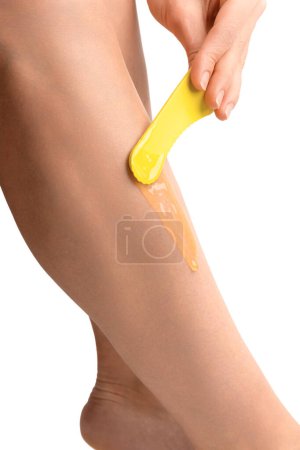 Foto de La chica hace depilación de las piernas de forma aislada. La mano de la niña aplica cera para depilación en la pierna sobre un fondo blanco. Arañando la piel. Cuidado corporal. Patas lisas. - Imagen libre de derechos