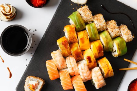 Téléchargez les photos : Ensemble rouleau avec saumon, avocat, crevettes et anguille sur une planche de pierre avec wasabi et sauce soja sur un fond gris, vue sur le dessus - en image libre de droit