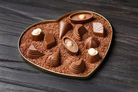 Téléchargez les photos : Bonbons au chocolat dans des pépites de chocolat dans une boîte en forme de coeur sur un fond en bois sombre close-up, Saint-Valentin. - en image libre de droit