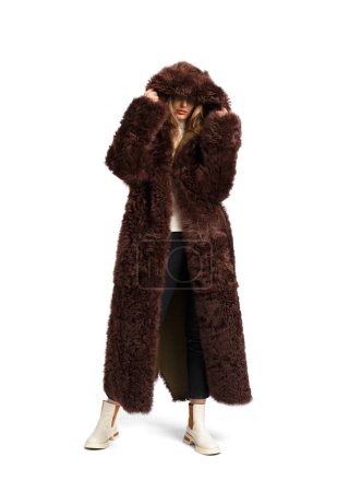 Foto de A young stylish girl in a luxurious long brown fur coat poses beautifully on a white background. Fashionable, stylish, comfortable outerwear, clothing advertising. - Imagen libre de derechos