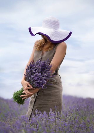 Foto de Girl in a dress and hat with a bouquet of lavender in her hands in a field of blooming lavender - Imagen libre de derechos