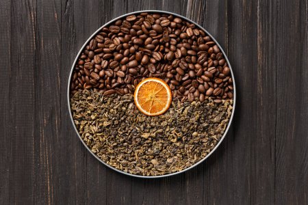 Foto de Green dry tea, coffee beans and a slice of dry orange in a round box on a dark wooden background top view. Conceptual composition of green tea and coffee beans on a dark background with space for text - Imagen libre de derechos
