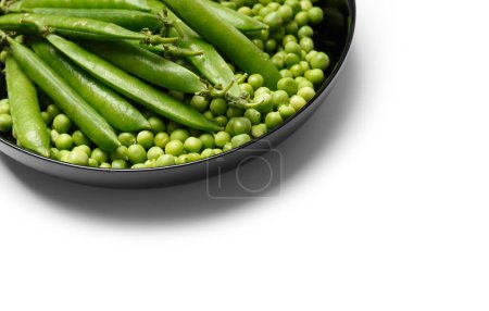 Foto de Guisantes verdes frescos en vainas y semillas de guisantes verdes peladas en un plato redondo negro, aislados sobre fondo blanco. Proteína vegetal, productos saludables. - Imagen libre de derechos