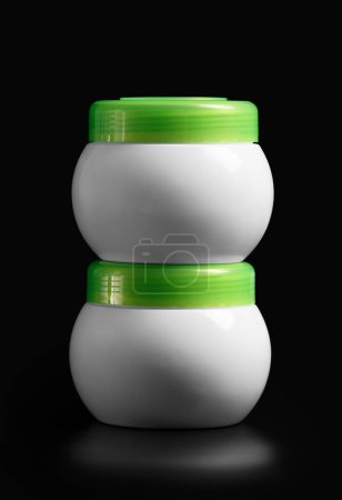Photo for A set of white jars with a green lid for cosmetic products for face and body skin care, hair, isolated on a black background. Packaging layout for cream, masks, scrub. Containers for hygiene products. - Royalty Free Image