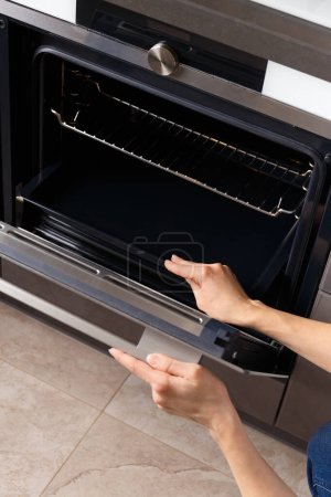 Photo for The girl opens the built-in oven door and takes out a baking sheet. Built-in oven with display in a modern kitchen interior. - Royalty Free Image