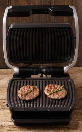 Téléchargez les photos : Les galettes de boeuf pour un hamburger sont frites avec des épices sur un gril électrique intelligent. Cuisiner des hamburgers faits maison. Ingrédients pour hamburgers. - en image libre de droit