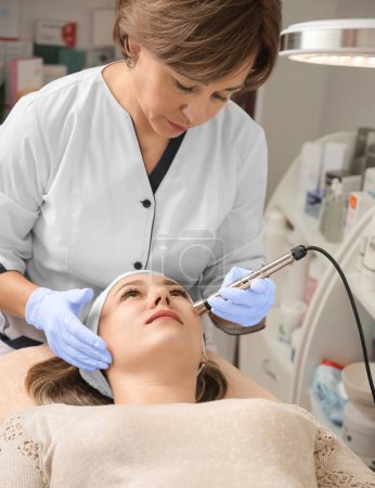 Téléchargez les photos : Rejuvenating facial therapy treatment at spa salon clinic. Young beautiful woman getting lifting anti-aging, face massage and skincare by electroporation facial therapy aesthetic cosmetology. - en image libre de droit