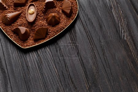Téléchargez les photos : Bonbons au chocolat se trouvent dans des pépites de chocolat dans une boîte sur un fond en bois sombre, gros plan. Chocolat praliné mélange de bonbons, espace de copie. - en image libre de droit