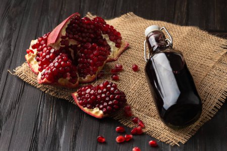 Photo for Ripe broken pomegranate, scattered large grains, freshly squeezed pomegranate juice in a transparent bottle on a wooden background. Creative composition of pomegranate and pomegranate juice. - Royalty Free Image