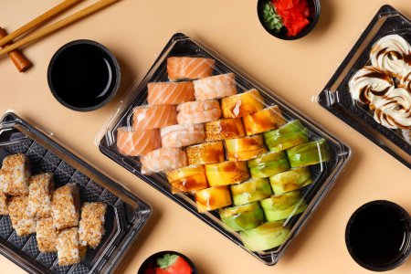 Téléchargez les photos : Un ensemble de rouleaux de sushi dans des emballages en plastique à emporter avec sauce soja, gingembre, wasabi et baguettes chinoises sur un fond clair, vue de dessus. Livraison de sushi dans un récipient en plastique - en image libre de droit