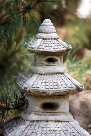 Photo for Decorative sculpture in the form of a Buddhist pagoda against the backdrop of beautiful greenery in the park. Japanese-style pagoda sculpture in the garden. - Royalty Free Image