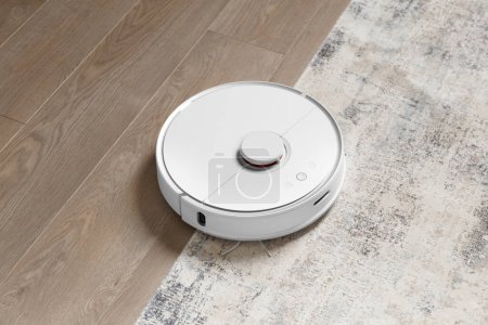 Robot aspiradora en la alfombra y en el laminado elimina el polvo. El concepto de un hogar inteligente, limpieza inalámbrica con una aspiradora inteligente de cualquier superficie.
