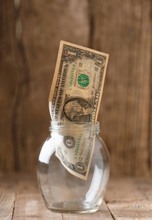 Photo for One dollar banknote in a glass jar on a wooden background, the concept of saving, money reserve, financial investment, cash accumulation, poverty, distrust in banks. - Royalty Free Image