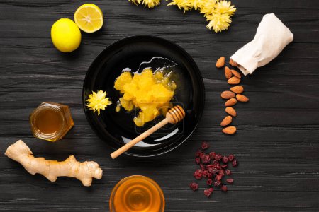 Photo for Crystallized honey in a black plate, honey in jars, almonds, lemon, ginger, dried berries on a dark textural background, top view. - Royalty Free Image