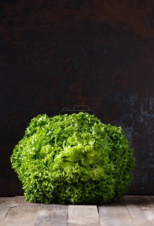 Téléchargez les photos : Grand bouquet de feuilles de laitue verte fraîche sur une table en bois et fond sombre, espace de copie. Aliments sains, source de minéraux et de vitamines. - en image libre de droit
