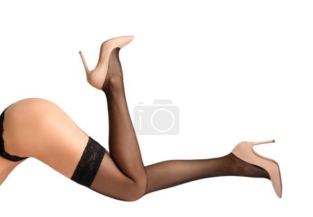 Téléchargez les photos : Jambes féminines fines en bas noirs avec une belle bande élastique ajourée et élégantes chaussures à talons hauts beige sur fond blanc, isolées. Gros plan sur les jambes gracieuses d'une fille en bas - en image libre de droit