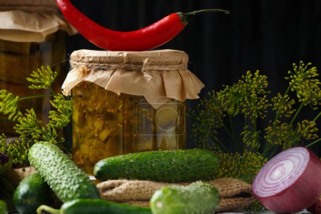 Foto de Pickled cucumbers in a jar, canned sliced cucumber salad, fresh gherkins, herbs and spices on a dark background, close-up. - Imagen libre de derechos